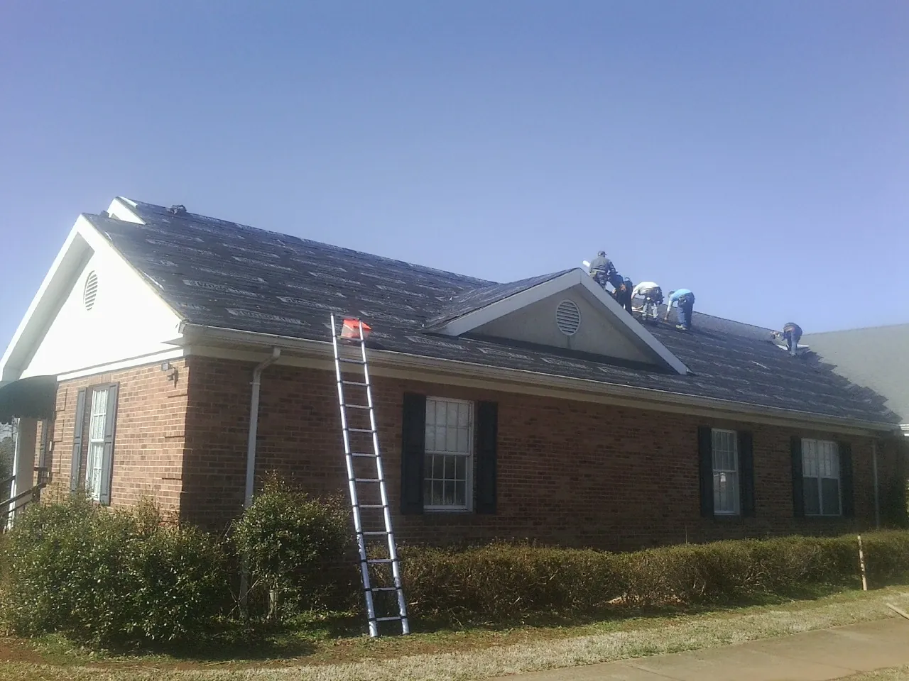 Crew tearing shingles off a brick ranch roof with a ladder set — Metal Roof Repair work by our crew in San Juan Capistrano