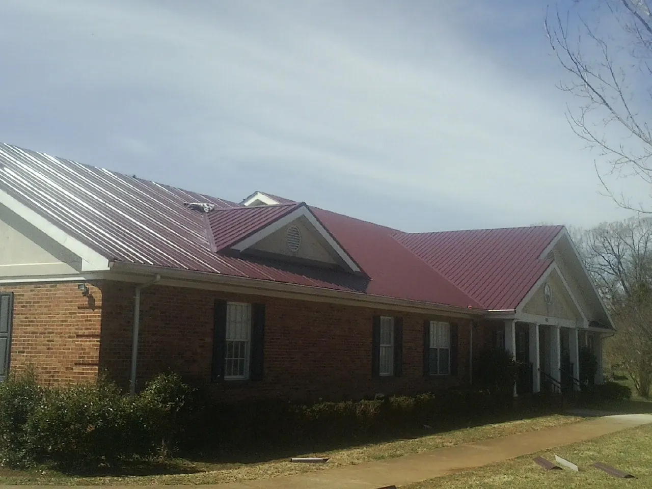 Red metal roof with gabled entries on a long brick building, from a Hail Damage Roof Repair job in San Juan Capistrano