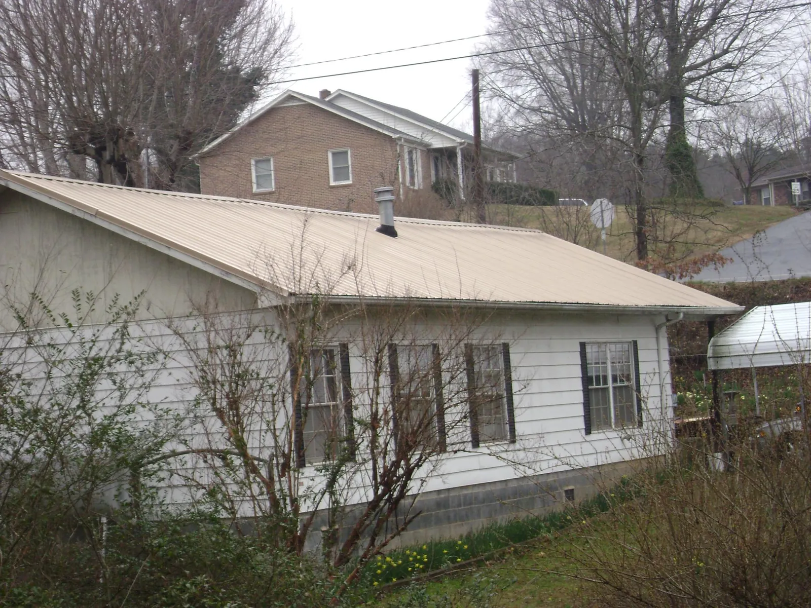 Tan metal roof on a white sided house set into a hillside — Commercial Roofing by Roofing Brothers in San Juan Capistrano